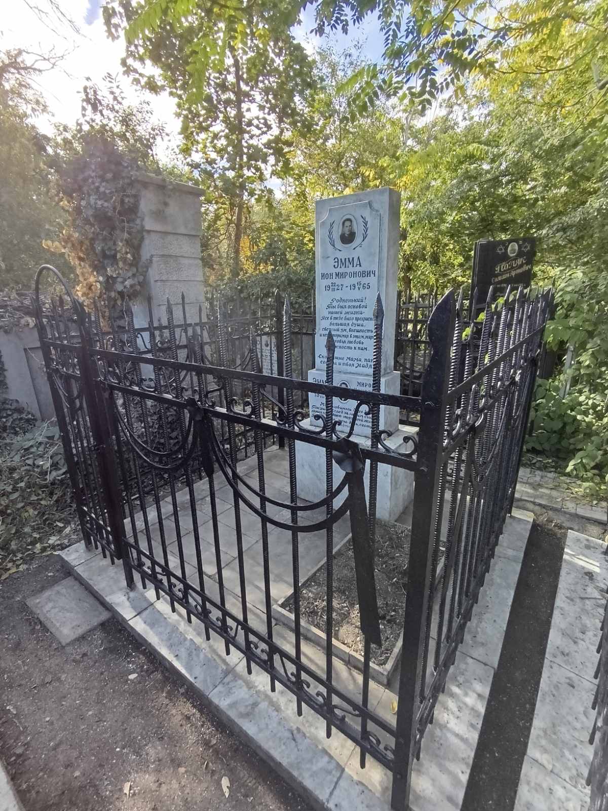 Tall marble headstone with Russian text and portrait, enclosed by a black wrought-iron fence.